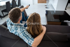 Back view of beautiful couple watching tv on sofa in living room